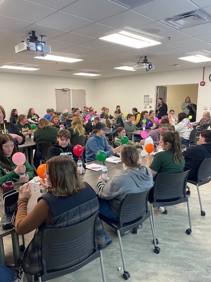 A group of youth seated at tables with balloons on top of bottles.